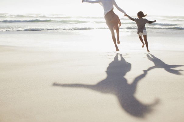 Blije moeder en kind lopen hand in hand met blote voeten over het strand op een zonnige dag en genieten van rust, ontspanning en quality time.